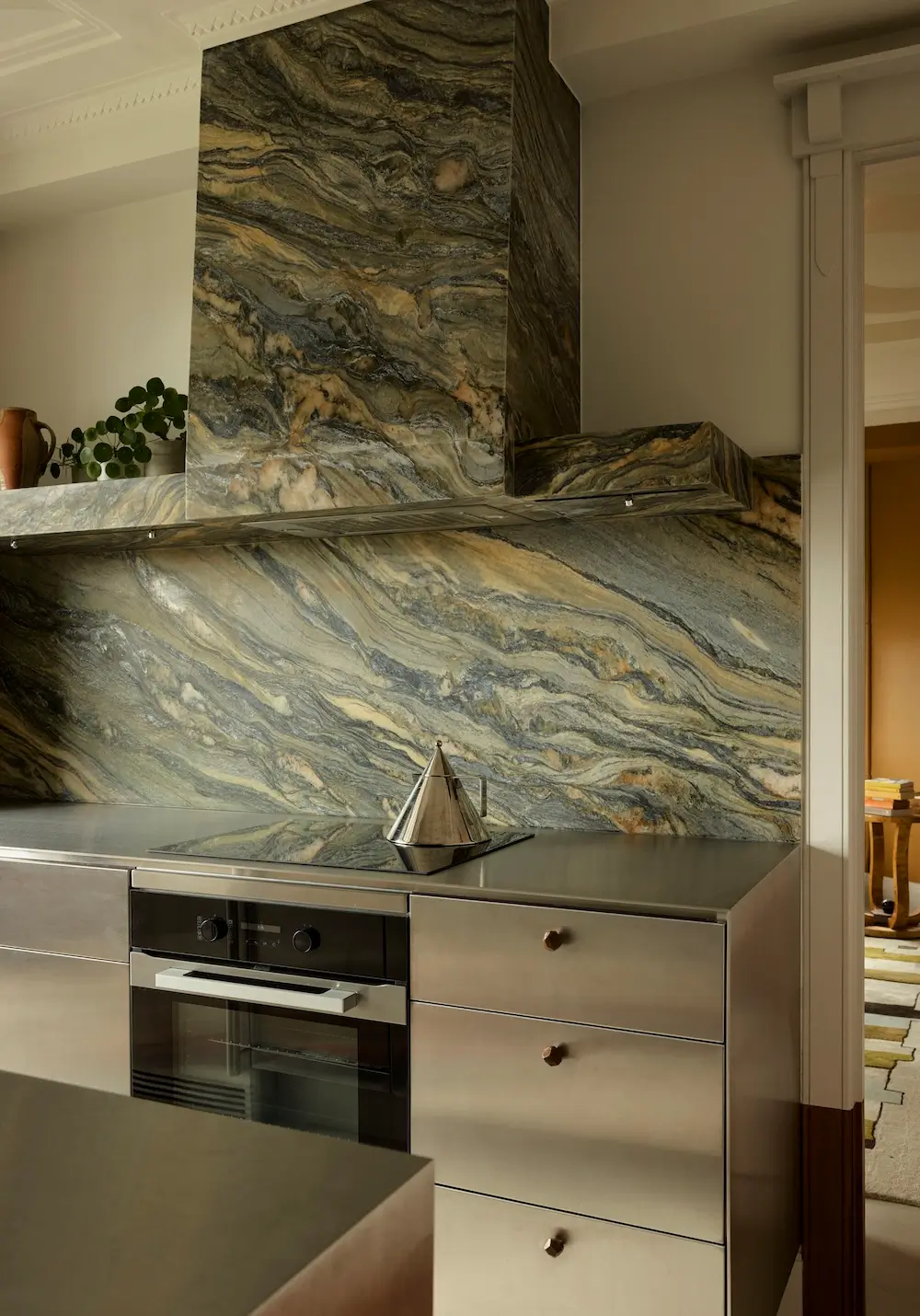 Kitchen in The Gentleman apartment by YSG Studio featuring Lauriana quartzite splashback, polished aluminium cabinetry, and a sculptural stone range hood.