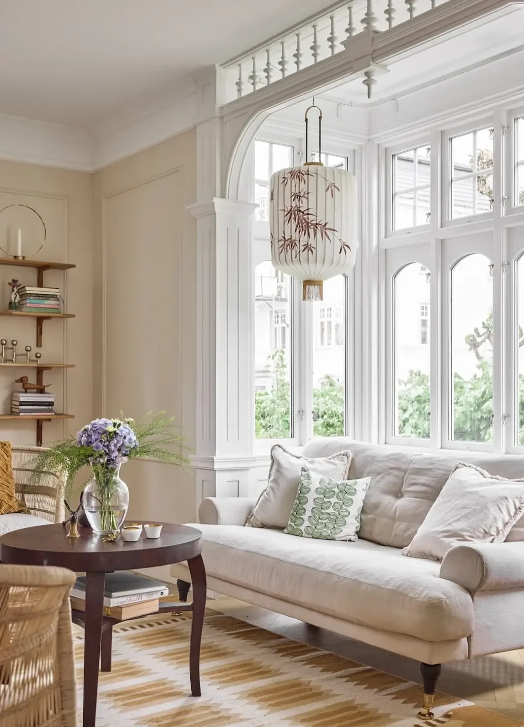 Elegant living room with a cream linen sofa, wicker armchairs, a dark wood coffee table, and large bay windows framed by decorative millwork.