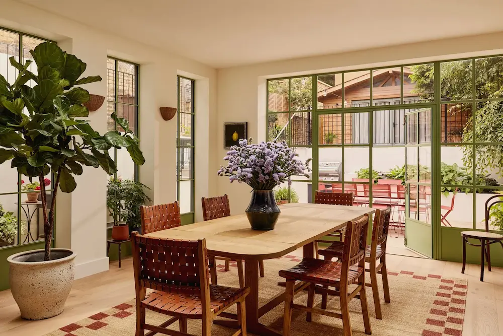 Dining room in Michelle Dockery's London Victorian home with an oak dining table, woven leather chairs, large steel-framed garden doors, and abundant natural light designed by Emma Ainscough.