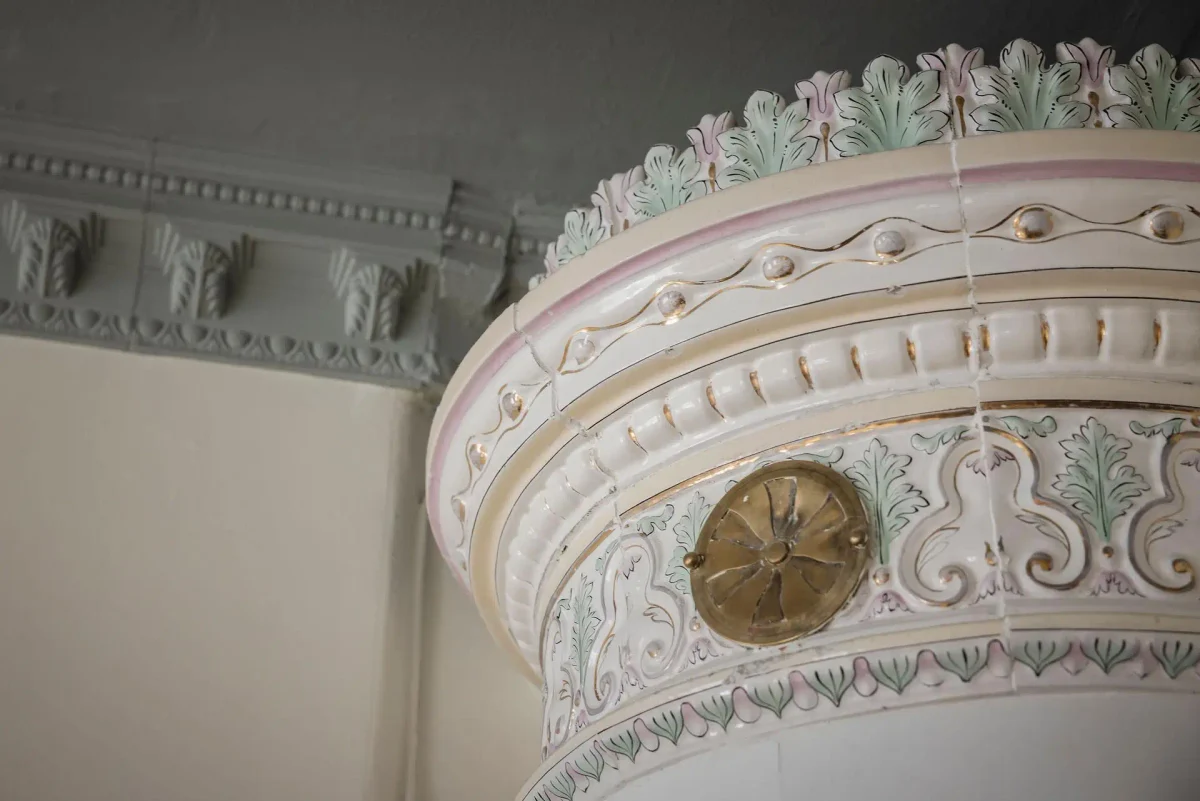 Close-up of an ornate antique Swedish tiled stove with delicate pink, green and gold floral details in a 1905 Gothenburg apartment.