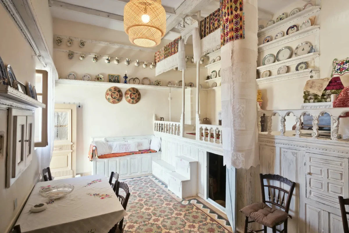 Traditional Karpathian interior in Menetes with white-painted carved woodwork, raised sleeping platform, antique plates, embroidered textiles and colorful woven rugs.
