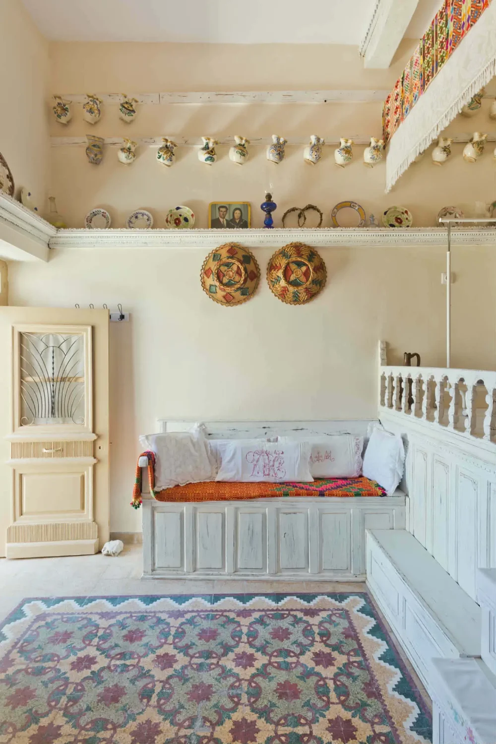 Traditional Karpathian interior with white-painted built-in seating, carved woodwork, antique ceramic plates, embroidered textiles and a colorful woven rug.
