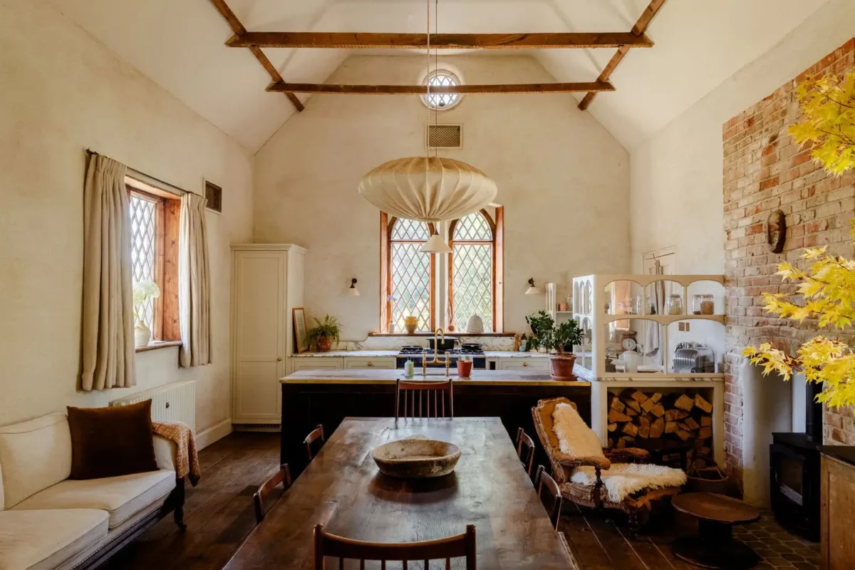 Beautiful historic home with exposed wooden ceiling beams, original brick walls, arched leaded-glass windows, aged wood floors, and a modern rustic kitchen.