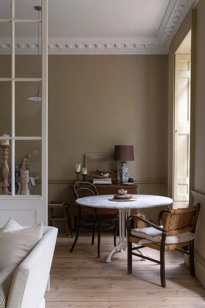 Elegant dining room with ornate original ceiling moldings, aged wooden floors, classic paneled doors, and a mix of antique and modern furniture.