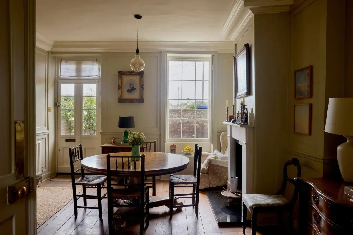 Charming traditional dining room with original wooden floors, decorative ceiling moldings, paneled walls, a classic fireplace, and antique furniture.